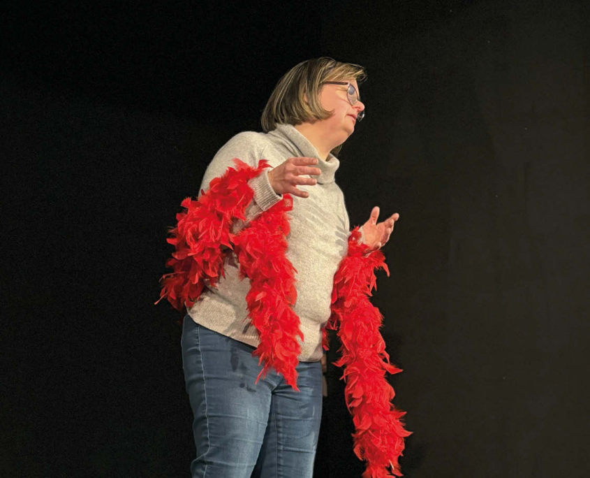 Una donna con un boa di piume rosse intorno alle spalle, recita la sua parte durante le prove di un spettacolo.