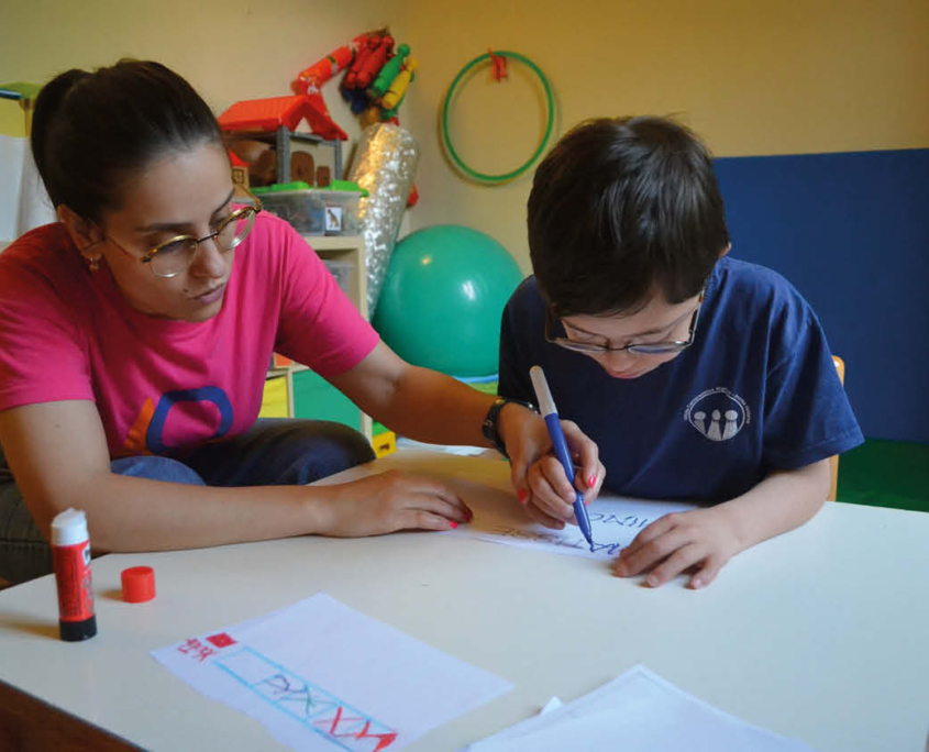 Un bambino esegue un esercizio di disegno, con il sostegno di una delle Neuropsicomotriciste accanto a lui.