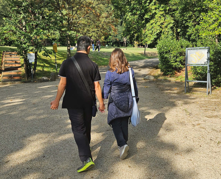 Due giovani di spalle, un uomo e una donna, si tengono per mano passeggiando in parco.