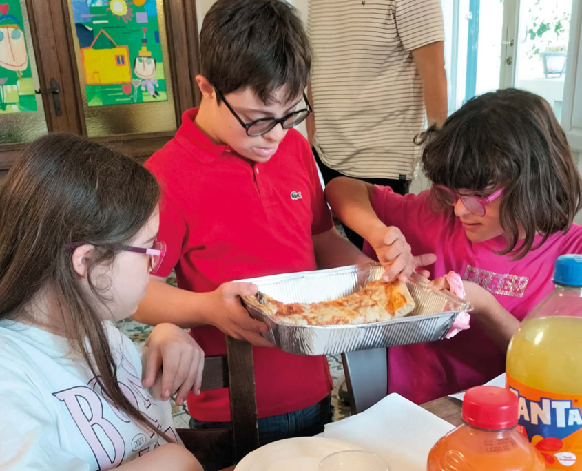 Tre persone, due ragazze e un ragazzo giovani, condividono una pizza durante l'attività dell'associazione.
